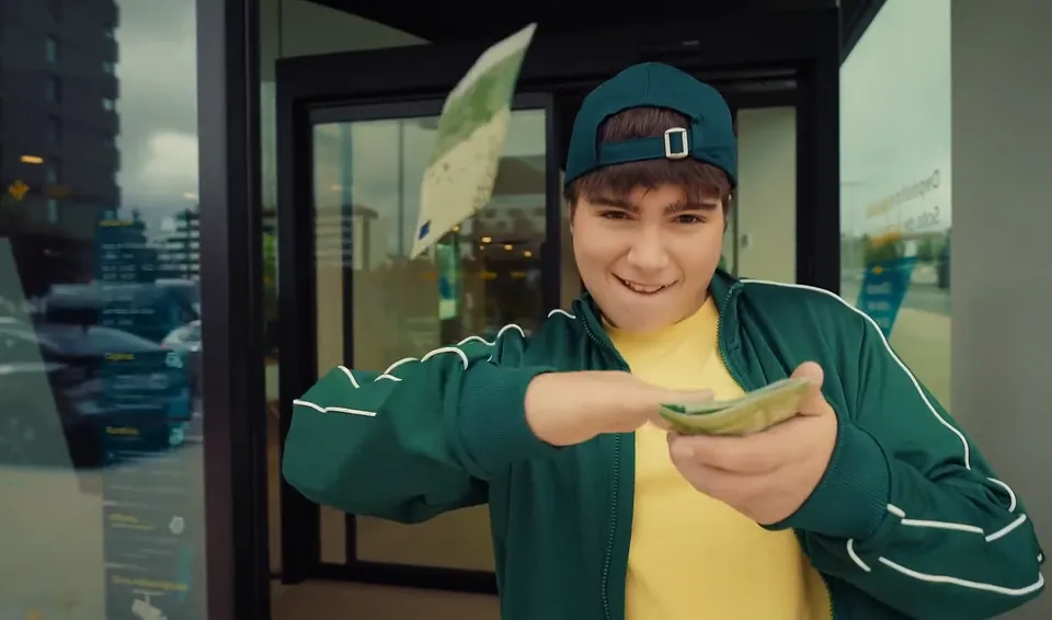 Un chico con gorra y chaqueta verde cuenta billetes ante una puerta de cristal.