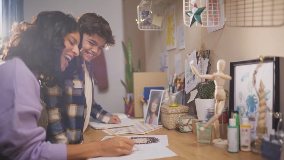 Fotograma: madre e hijo en una mesa con dibujos y fotos.