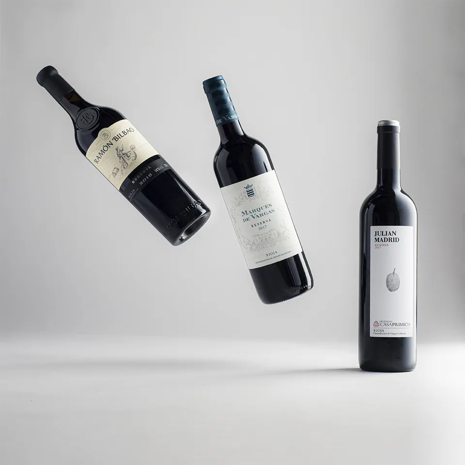 Tres botellas de vino tinto que flotan sobre fondo gris.