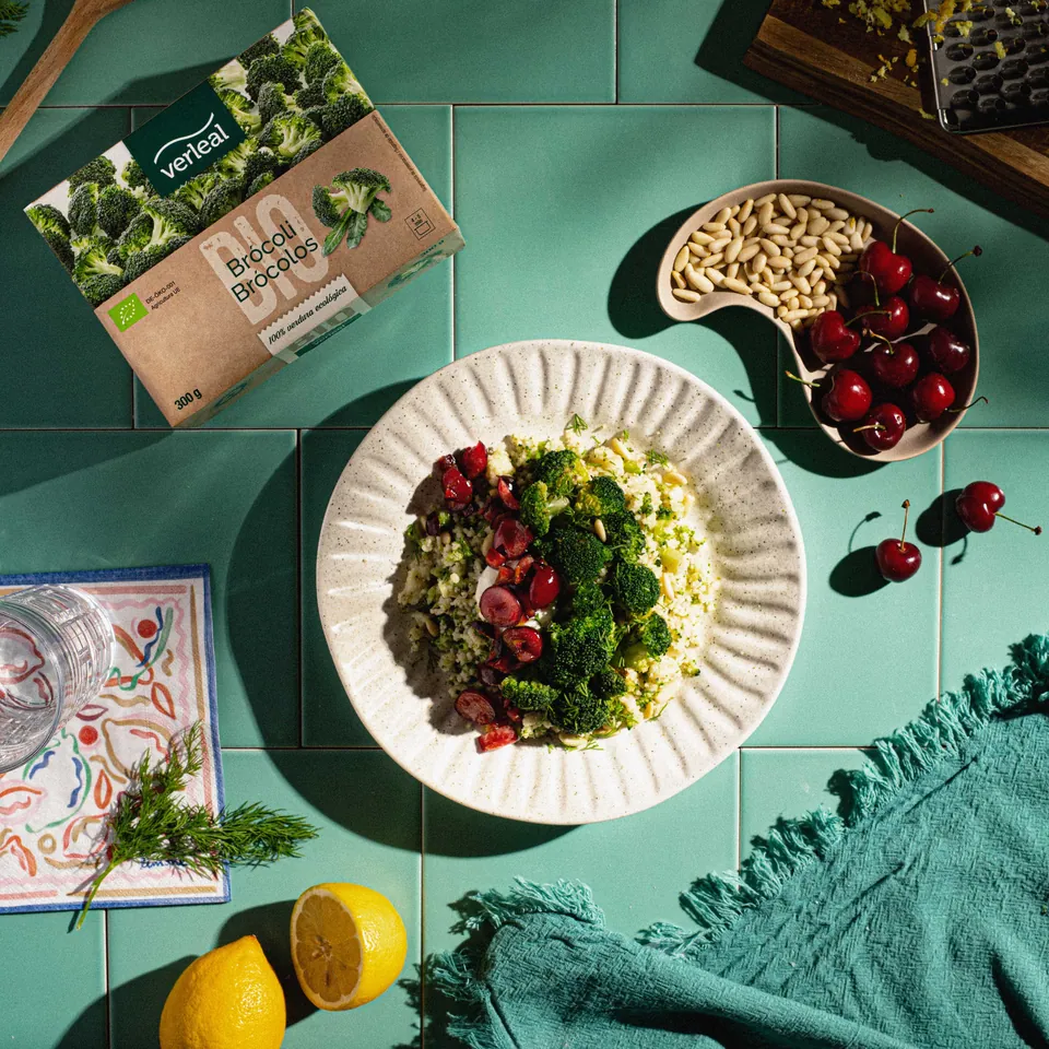Plato de verduras visto desde arriba sobre azulejo verde, con cerezas y limones.